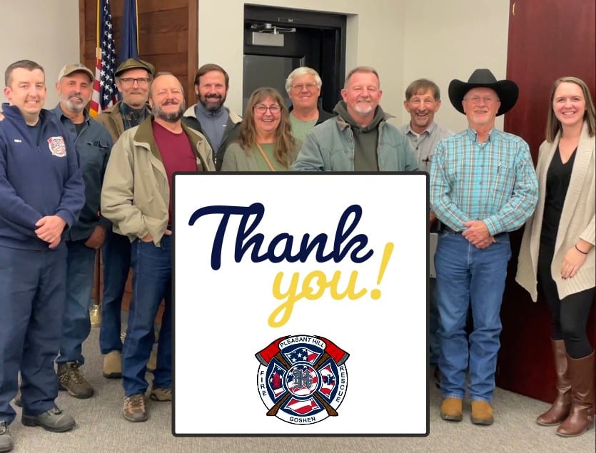 A group of people stand smiling at the camera; in front is a sign that reads "Thank you!" with the Pleasant Hill Goshen Fire and Rescue Logo.
